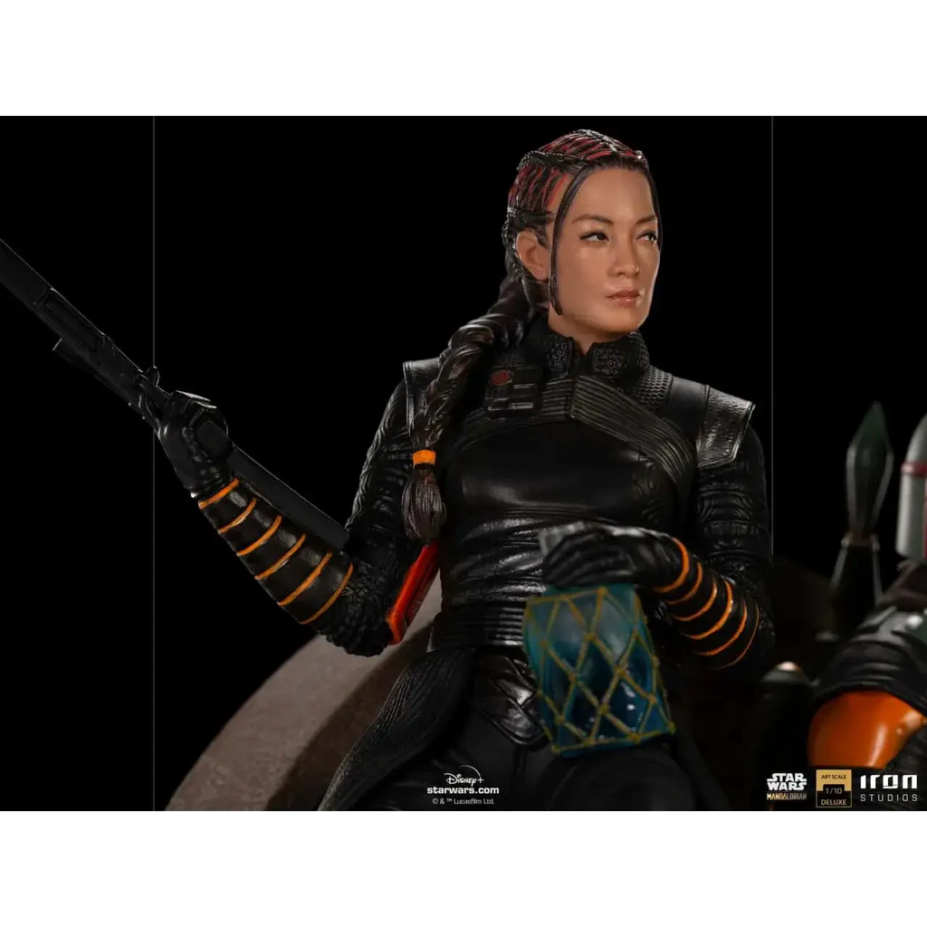 Svart rustad figur med flätat hår och orange accenter, håller blastergevär i Boba Fett och Fennec Shand deluxe 1/10 staty