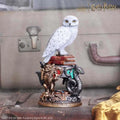 Vit snöugglafigur av Hedwig från Harry Potter på röda böcker med gyllene lejon och silverorm