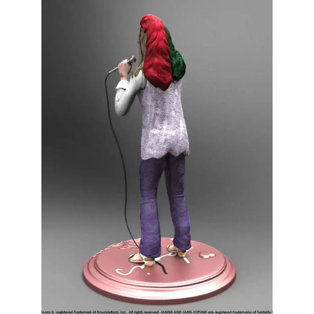 Janis Joplin Rock Iconz staty med rött och grönt flätat hår, vit spetsblus och lila byxor på rosa bas