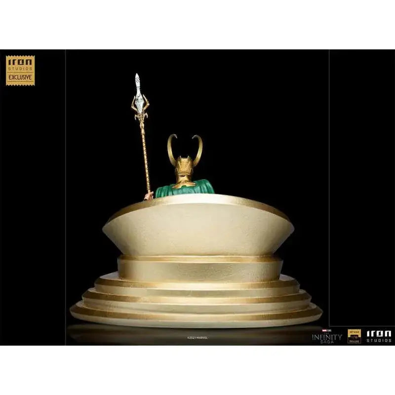 Guld Loki-statue med grön mantel, hornhjälm och spjut på gul bas