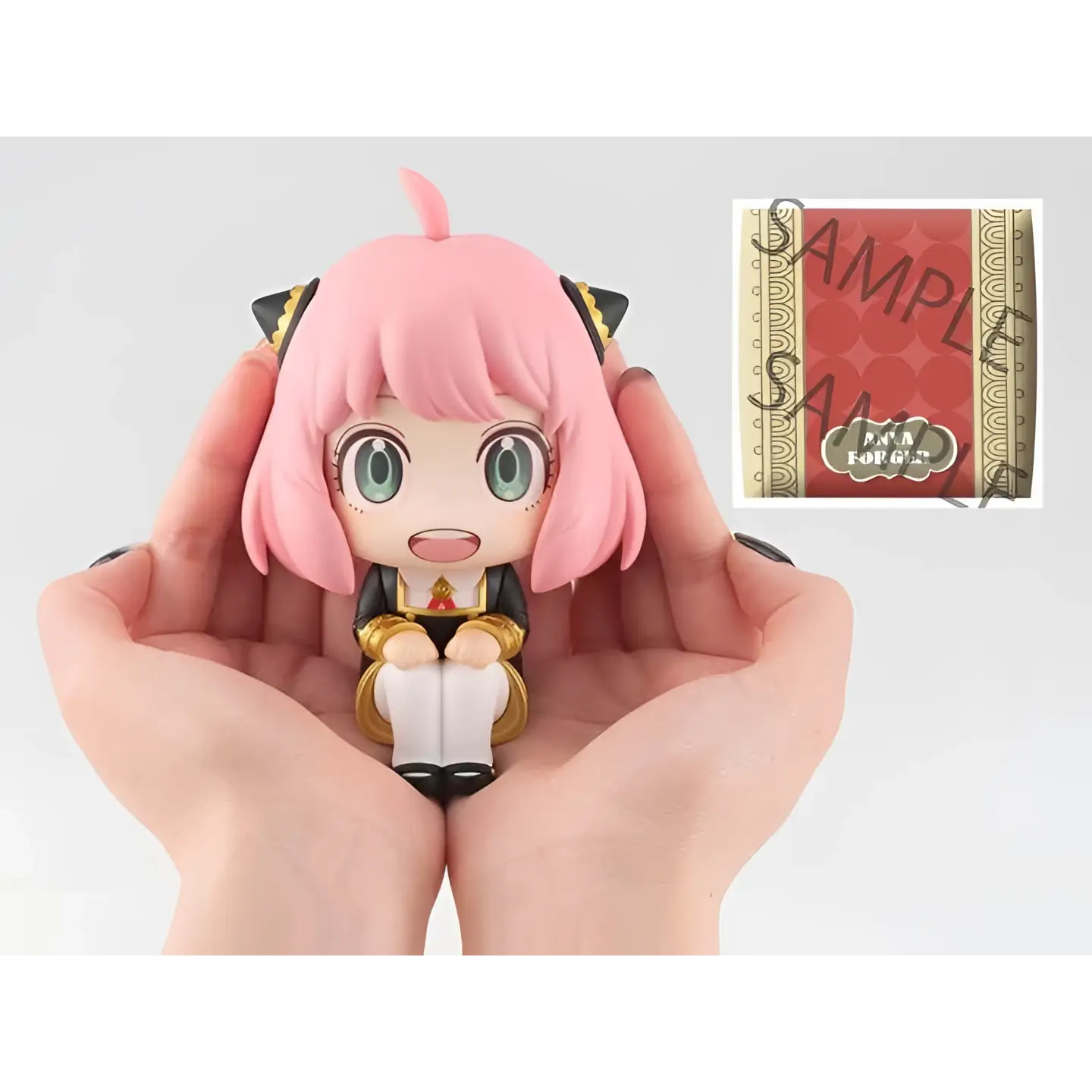 Rosa hårup Anya Forger chibi-figur med gröna ögon, svart-guld outfit i händer
