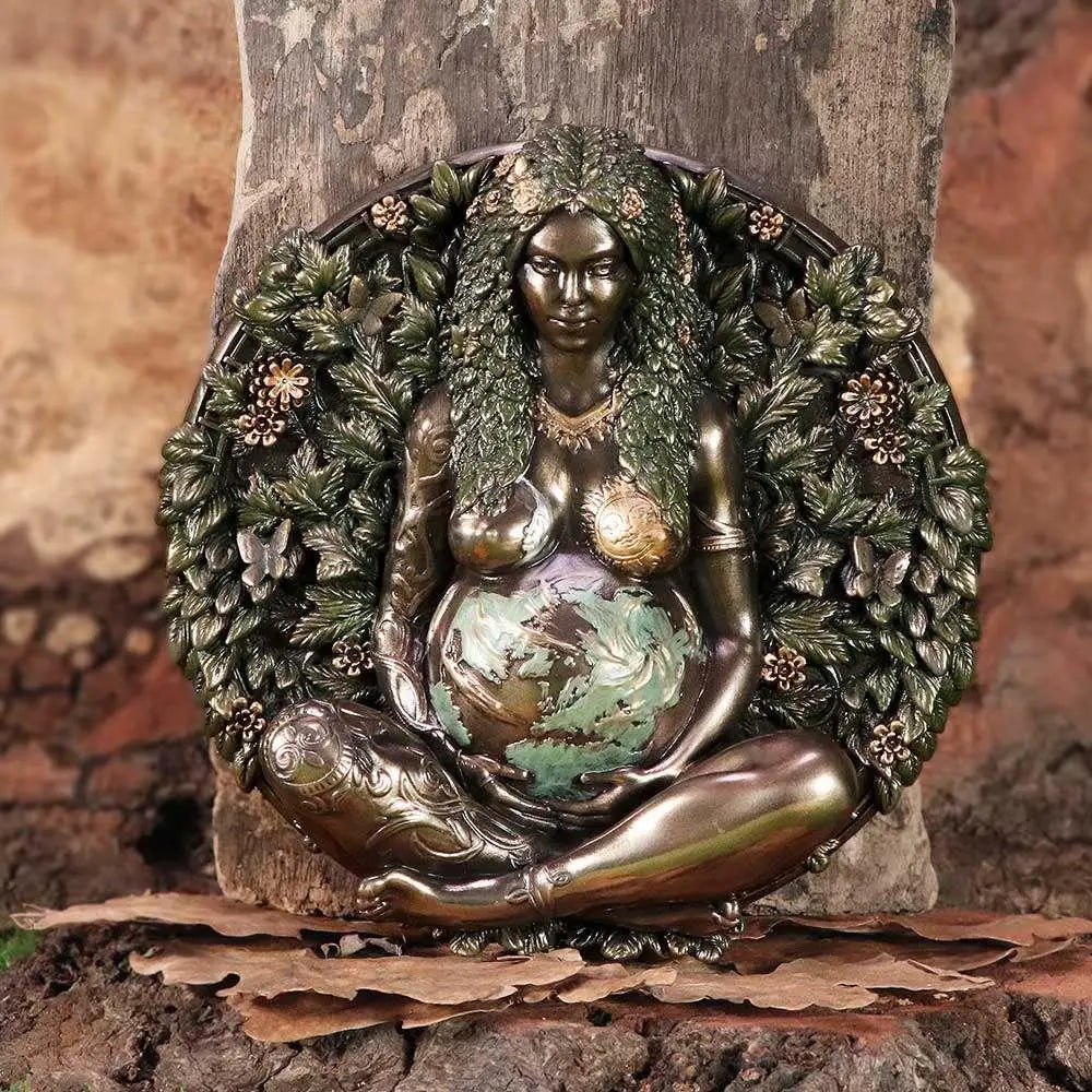 Bronsfärgad figur av gravid gudinna med grönt bladigt hår och blomsterkrans, hållande jordklotmage. Moder Jord väggplakett