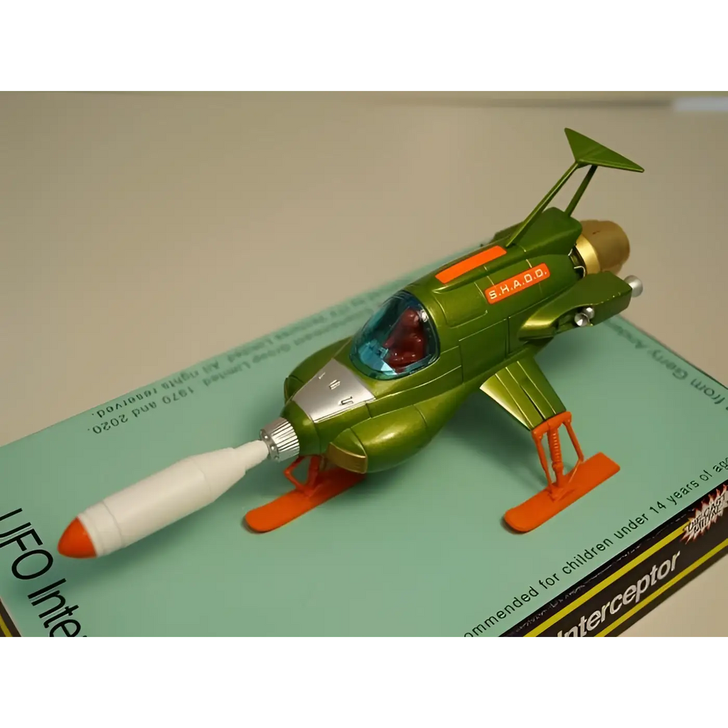 Retro UFO Interceptor diecast leksaksrymdskepp i grönt och orange med silverkabin, röd pilot och Shado-text