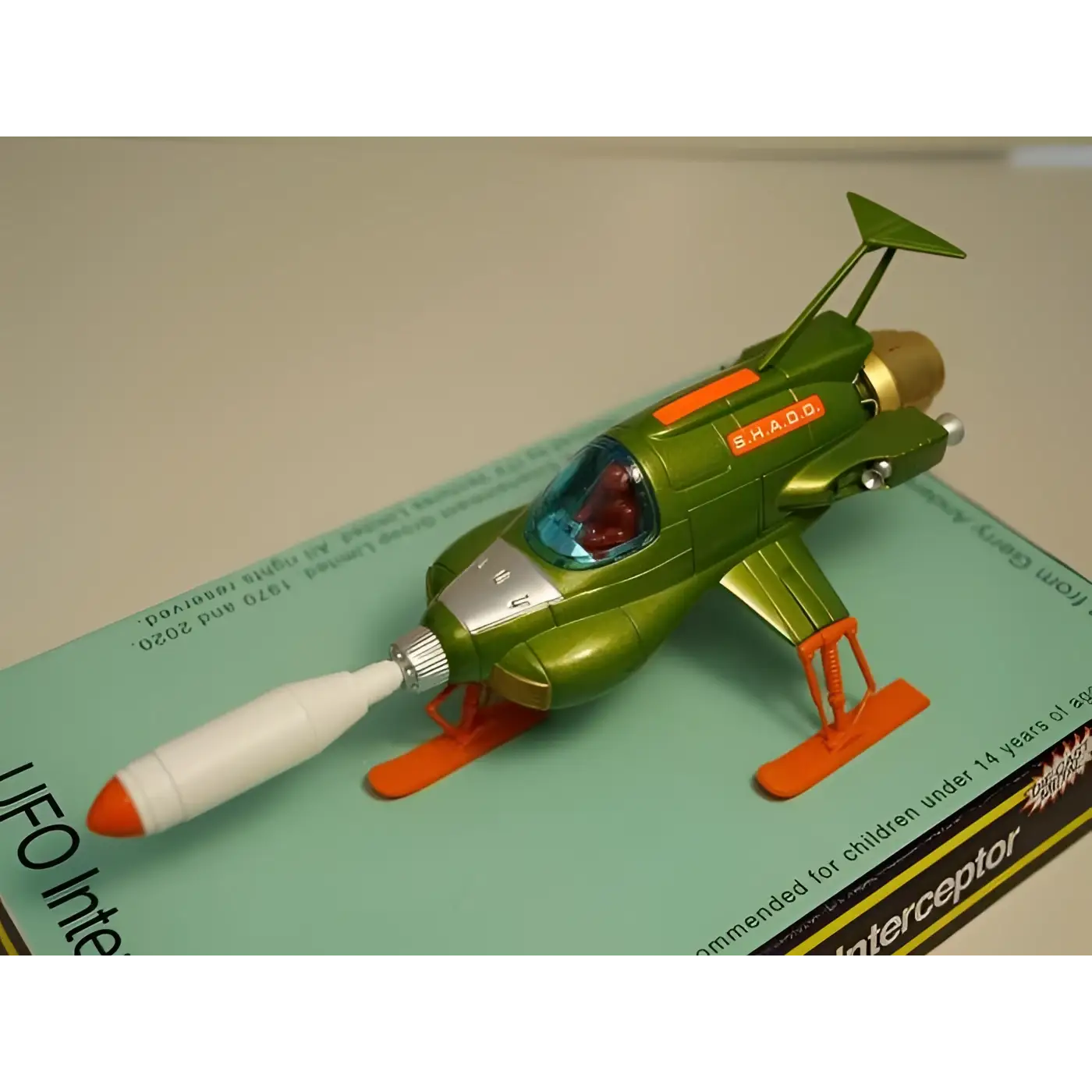 Retro UFO Interceptor diecast leksaksrymdskepp i grönt och orange med silverkabin, röd pilot och Shado-text