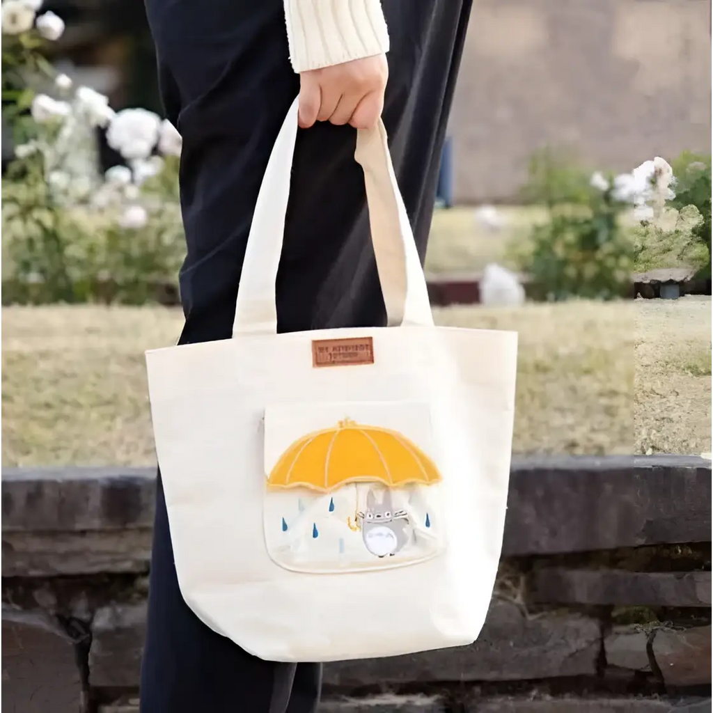 Beige canvasväska med Totoro-broderi under gul paraply och fodral