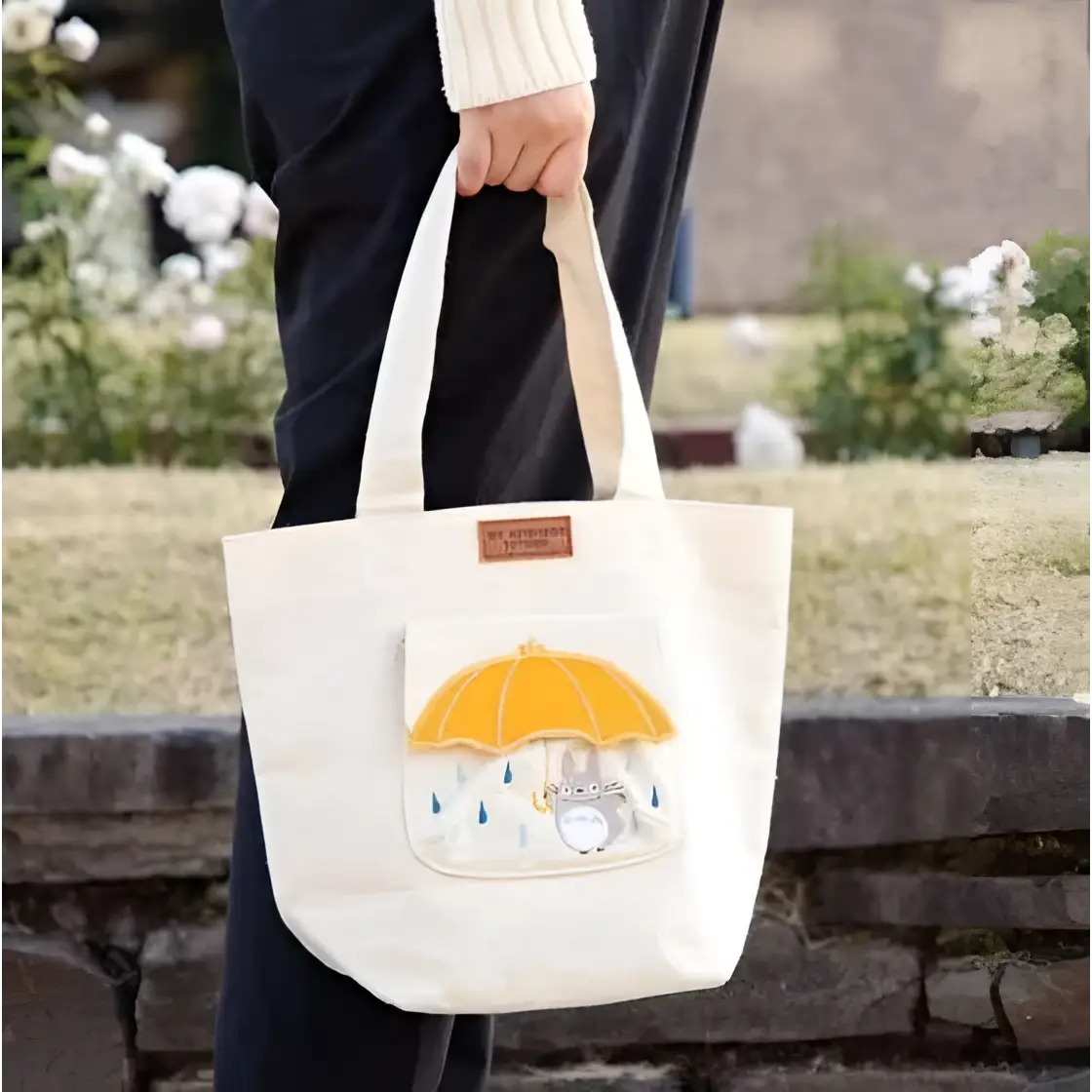 Beige canvasväska med Totoro-broderi under gul paraply