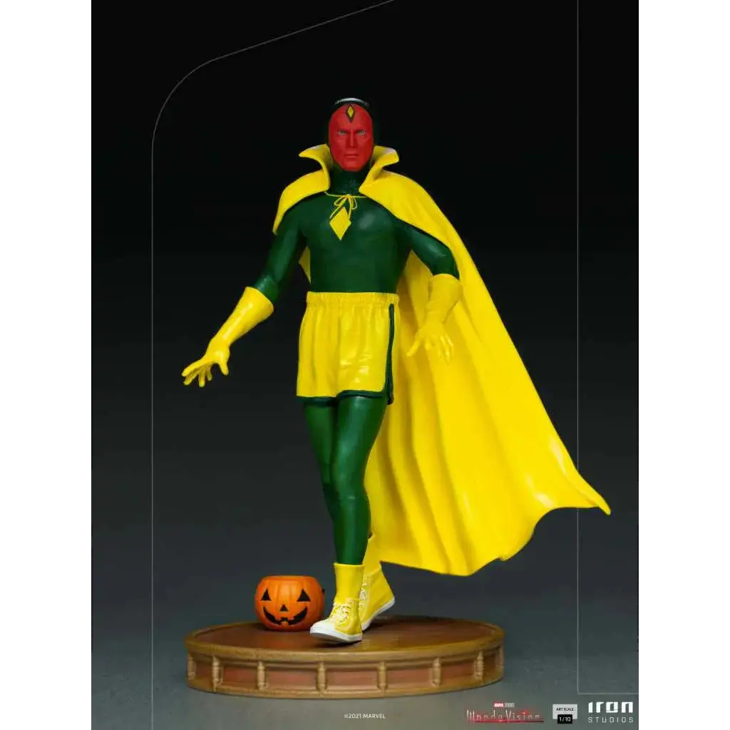 Wandavision Halloween Vision-staty med rött ansikte, grön-gul kostym, fladdrande mantel på rund sockel bredvid snidad pumpa